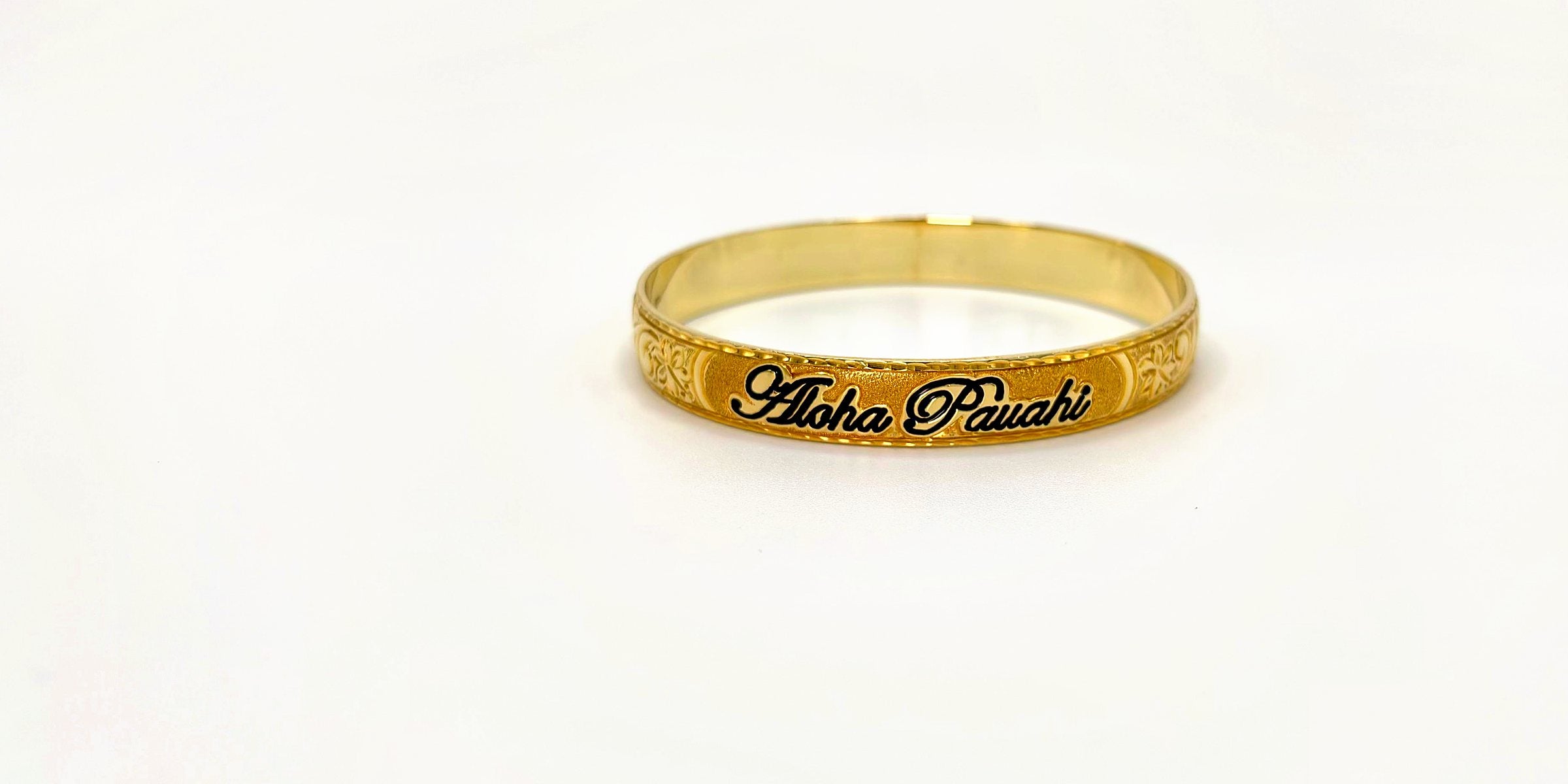 Aloha Pauahi gold Hawaiian heirloom bangle with the black enamel Aloha Pauahi script, on a plain light backdrop.