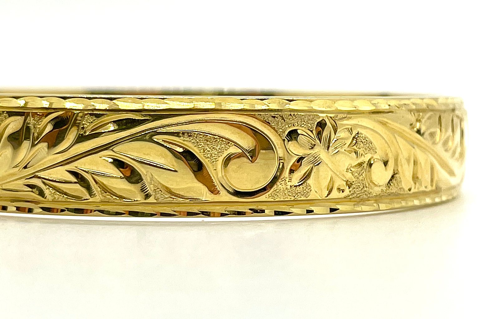 Detail of the hand engraved scroll and plumeria pattern on a gold Hawaiian heirloom bangle.