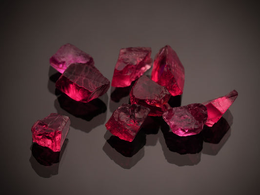 Vibrant red ruby gemstones on a dark reflective surface — July's birthstone