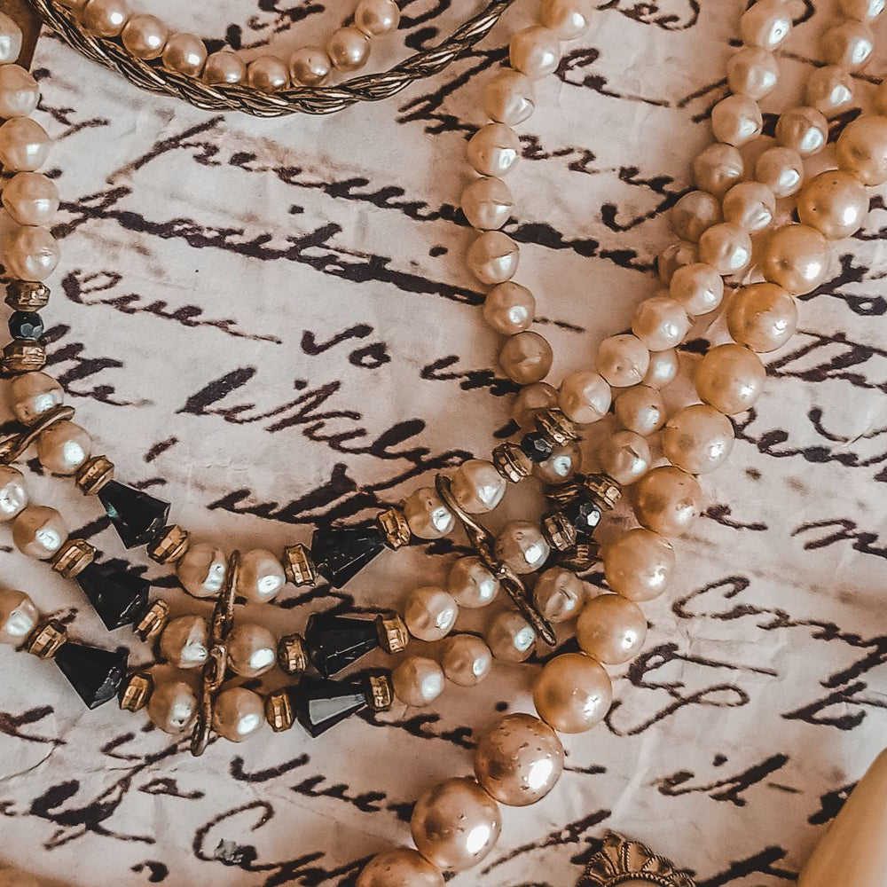 Antique pearl necklace and earrings resting on a vintage handwritten letter, representing inherited heirloom jewelry