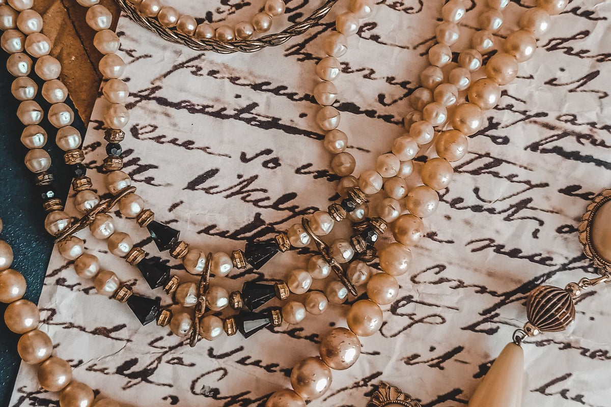 Antique pearl necklace and earrings resting on a vintage handwritten letter, representing inherited heirloom jewelry