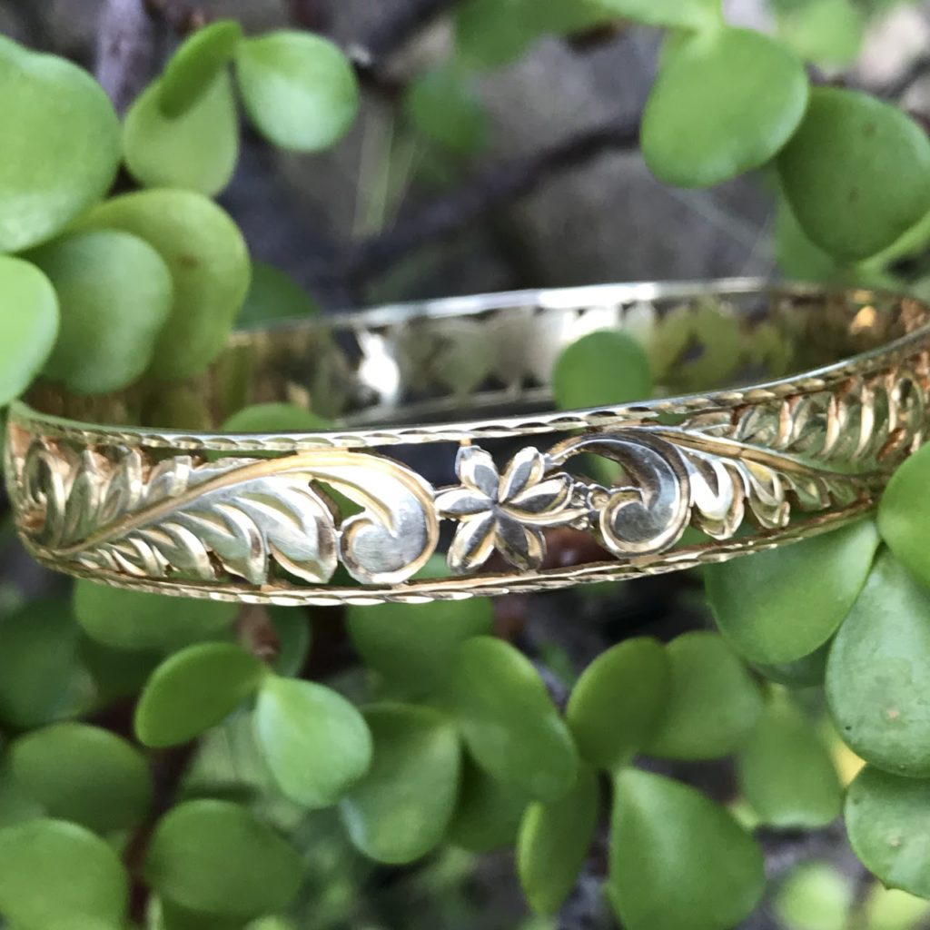 Aloha Pauahi 10mm solid gold filigree Hawaiian heirloom bangle with open scroll and blossom cutouts among jade plant leaves, handcrafted by Jewel Box Hawaii in Honolulu.