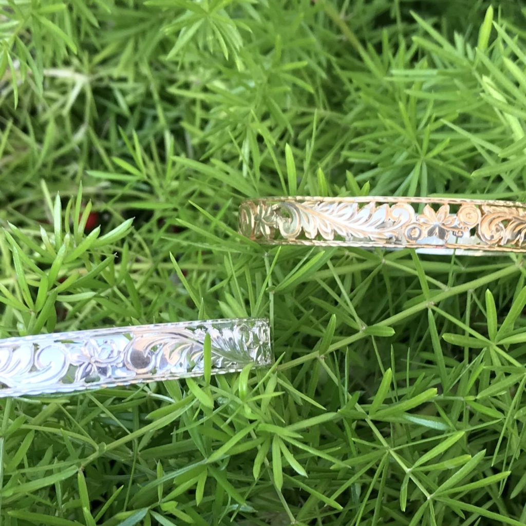 Two Aloha Pauahi 10mm sterling silver filigree Hawaiian heirloom bangles with open scrollwork lying in grass, handcrafted by Jewel Box Hawaii in Honolulu.