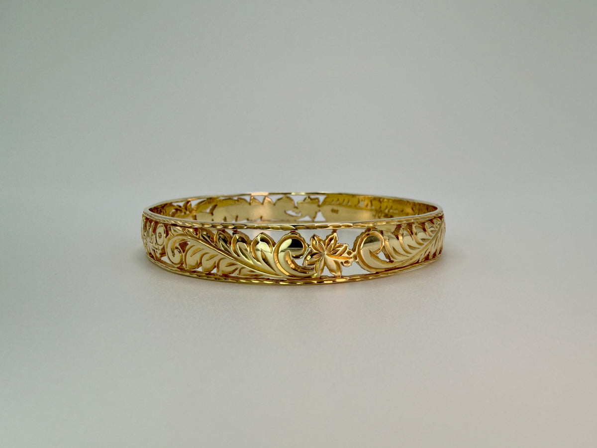 Aloha Pauahi gold Hawaiian heirloom bangle bracelet with wide pierced openwork band in close-up front-facing view showing bold raised maile-leaf fronds and plumeria blossom in center with inner rim visible at top, handcrafted by Jewel Box Hawaii in Honolulu.