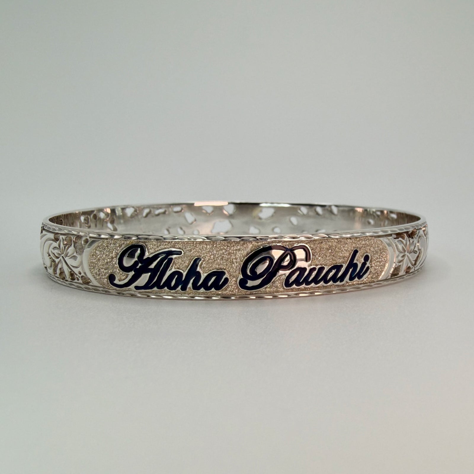 Aloha Pauahi sterling silver bangle with the name in black enamel script between pierced floral side panels, handmade and hand engraved in Hawaii.