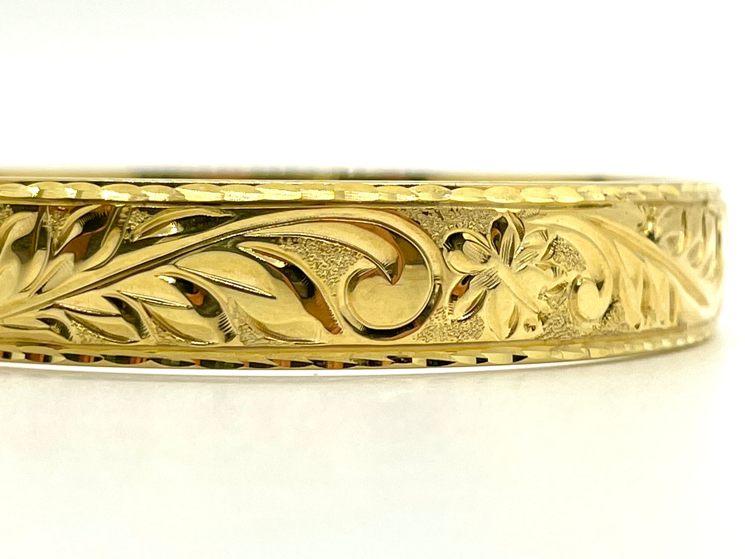 Detail of hand engraved scroll and plumeria pattern on a gold Hawaiian heirloom bangle, handcrafted by Jewel Box Hawaii in Honolulu.