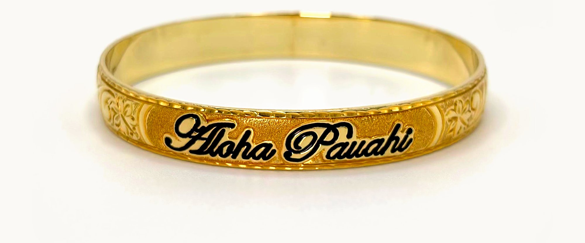 Aloha Pauahi gold Hawaiian heirloom bangle with the black enamel Aloha Pauahi script, on a plain light backdrop.