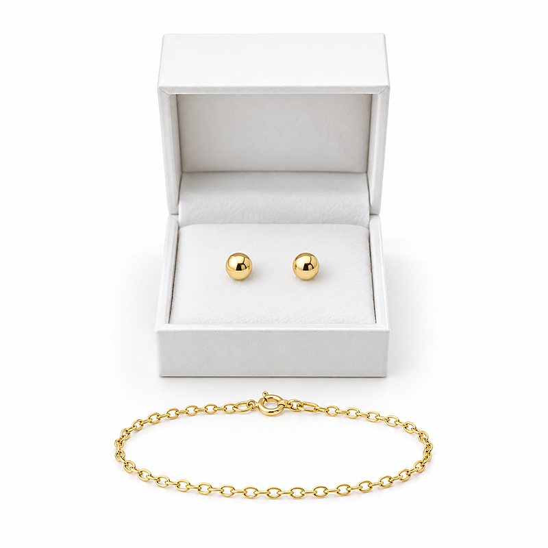 A small open white gift box holding a pair of yellow gold ball stud earrings, with a fine yellow gold chain bracelet curved in front of it.