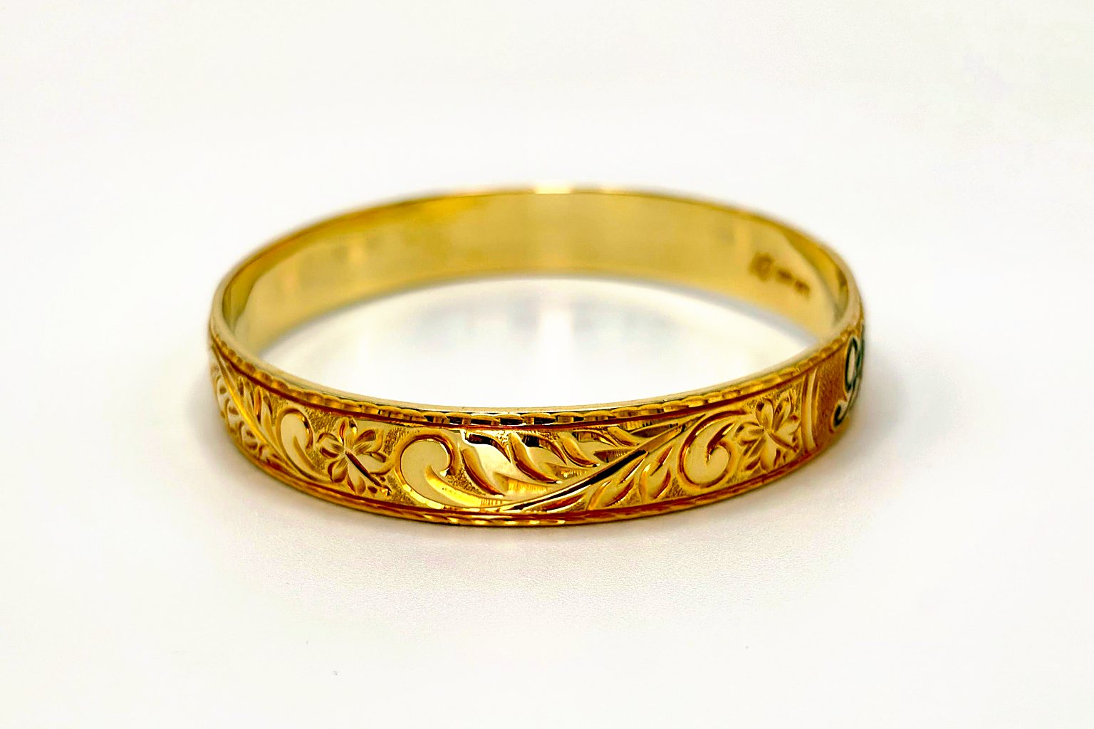 Aloha Pauahi gold Hawaiian heirloom bangle with a solid hand engraved band, front view on a plain light backdrop.
